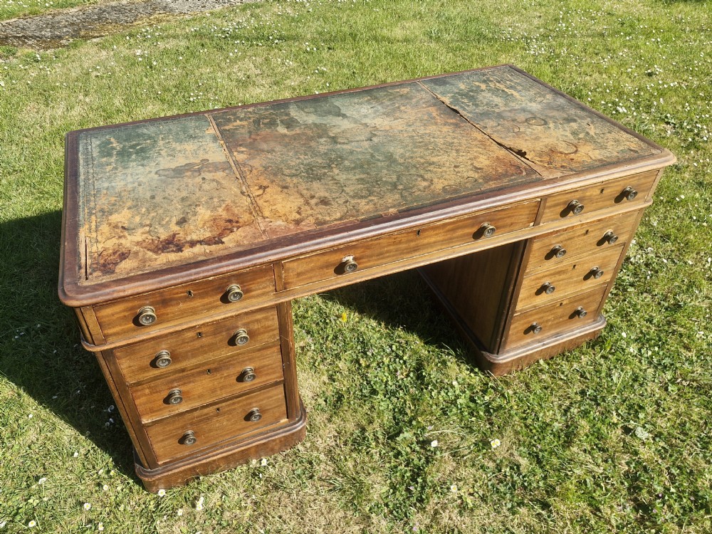 A late Victorian mahogany kneehole desk featuring twin pedestals with drawers, a plinth base, and a worn leather writing surface. View V