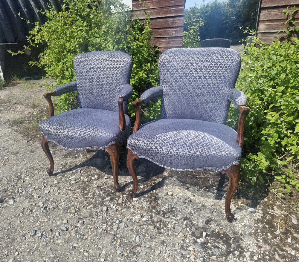 A pair of open arm armchairs with carved mahogany cabriole legs and blue patterned fabric upholstery.