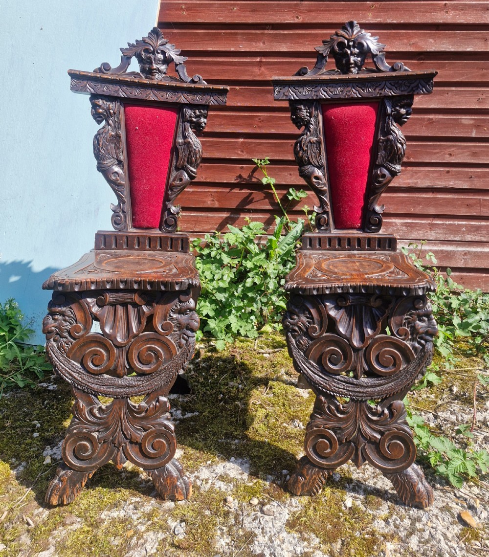 A pair of 19th-century carved walnut hall chairs featuring relief mascarons, scrollwork legs, and red velvet backrest panels. View II
