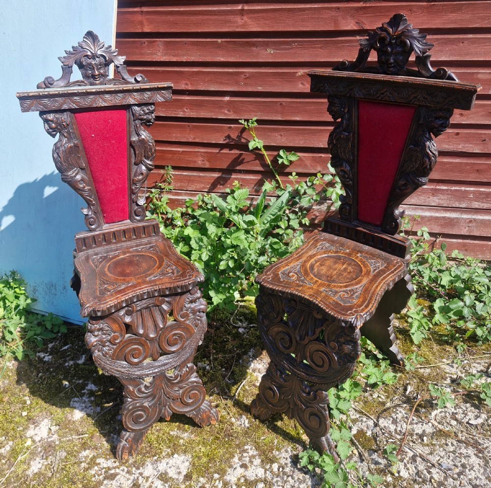 A pair of 19th-century carved walnut hall chairs featuring relief mascarons, scrollwork legs, and red velvet backrest panels. View VI