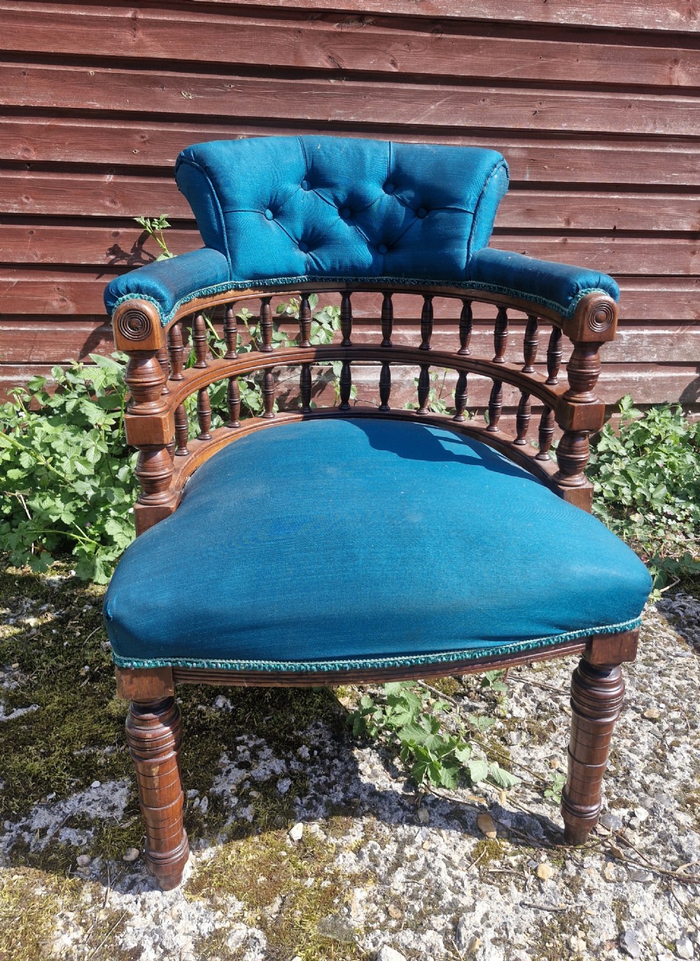 A Victorian wooden desk armchair featuring teal blue button-backed upholstery, a curved spindle gallery, and turned legs.