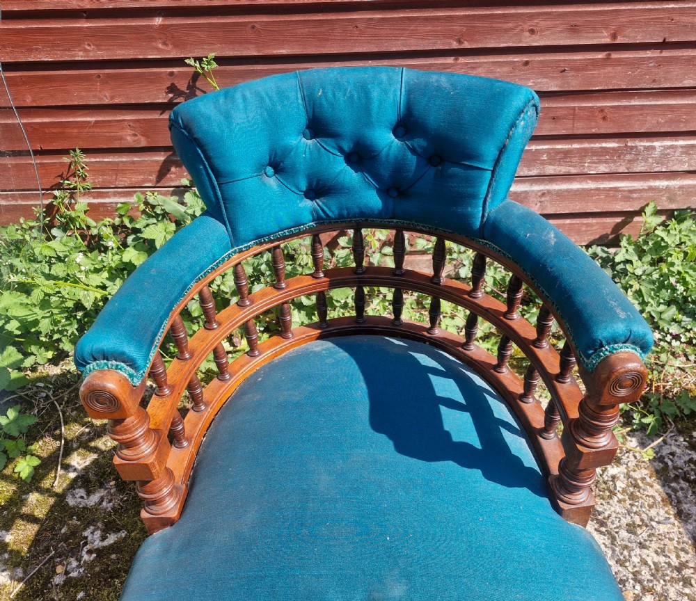 A Victorian wooden desk armchair featuring teal blue button-backed upholstery, a curved spindle gallery, and turned legs. View VI