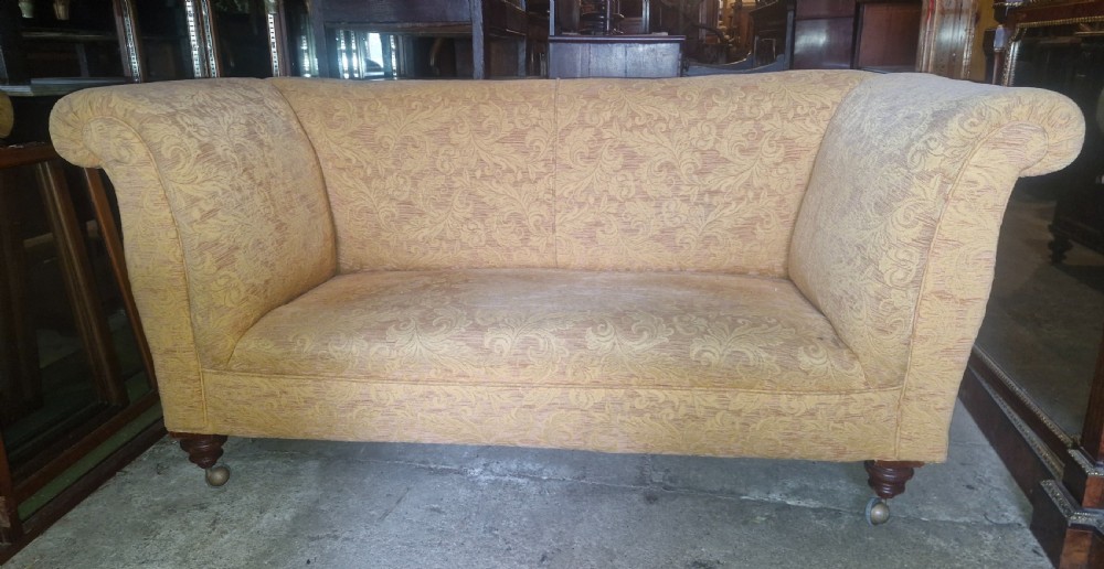 A late Victorian two-seater sofa upholstered in a yellow floral patterned fabric with scrolled arms and turned walnut legs on brass castors.