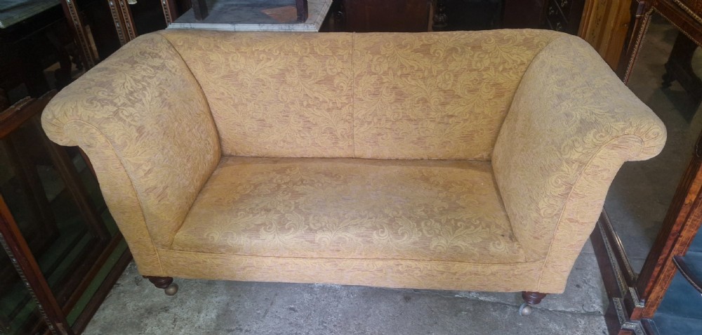 A late Victorian two-seater sofa upholstered in a yellow floral patterned fabric with scrolled arms and turned walnut legs on brass castors. View II