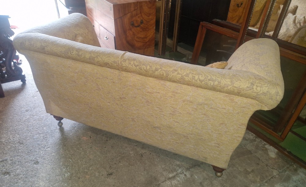 A late Victorian two-seater sofa upholstered in a yellow floral patterned fabric with scrolled arms and turned walnut legs on brass castors. View IV