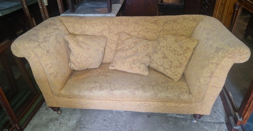 A late Victorian two-seater sofa upholstered in a yellow floral patterned fabric with scrolled arms and turned walnut legs on brass castors. View VIII