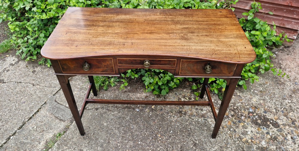 An antique Regency mahogany side table featuring a curved front apron, three inlaid drawers with turned brass handles, and square tapered legs connected by stretchers. View III