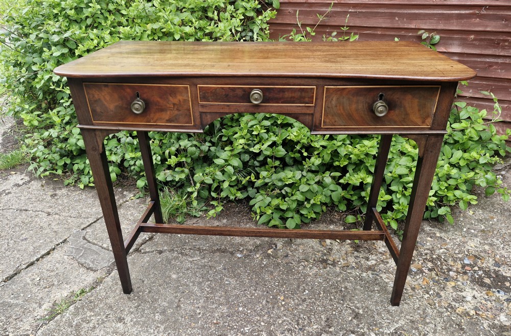 An antique Regency mahogany side table featuring a curved front apron, three inlaid drawers with turned brass handles, and square tapered legs connected by stretchers. View VI