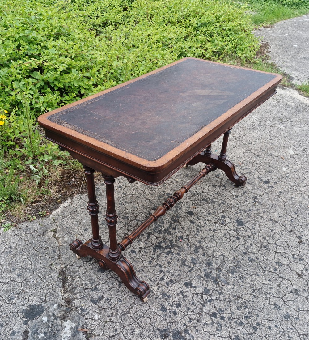 A mid-Victorian rectangular walnut library table featuring an inset dark leather top, turned dual end supports, a central turned stretcher, and carved legs with castors. View II