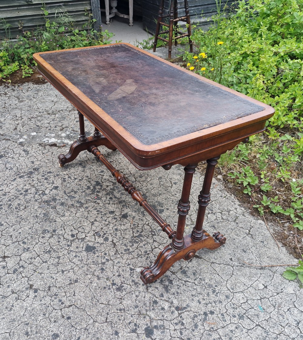 A mid-Victorian rectangular walnut library table featuring an inset dark leather top, turned dual end supports, a central turned stretcher, and carved legs with castors. View III