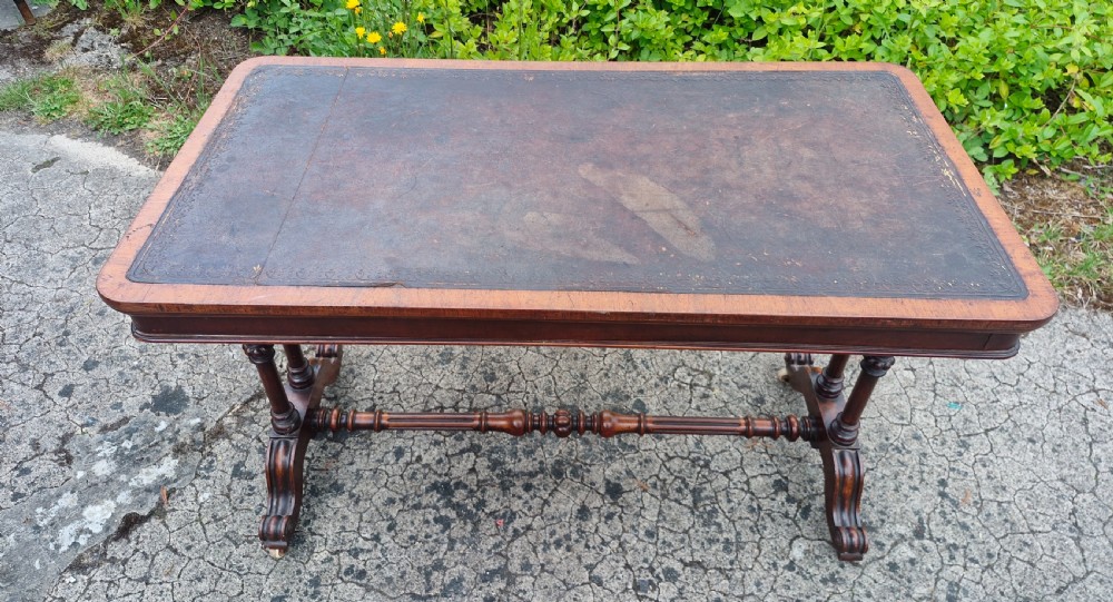 A mid-Victorian rectangular walnut library table featuring an inset dark leather top, turned dual end supports, a central turned stretcher, and carved legs with castors. View IV