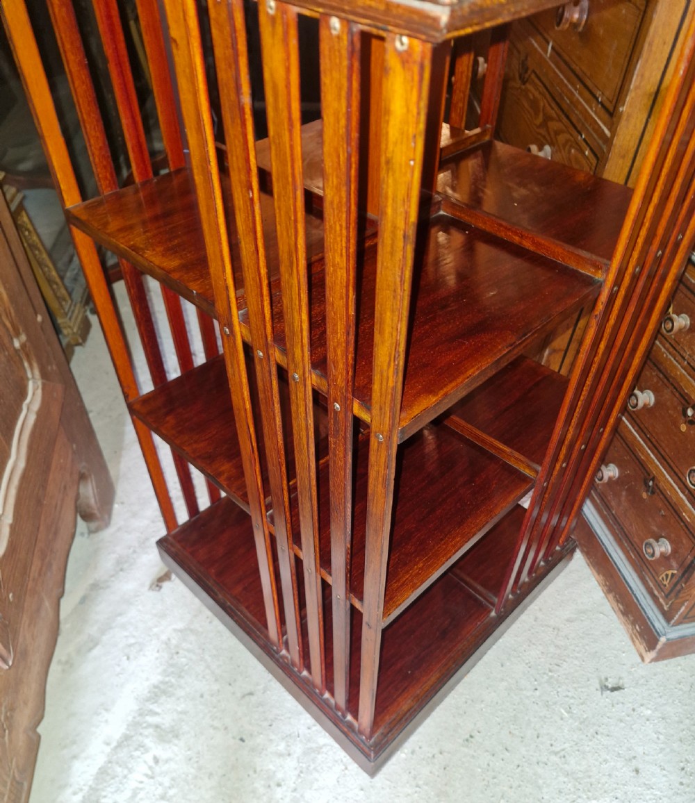 An Edwardian dark walnut revolving bookcase featuring a square moulded top, open internal tiers, and vertical slatted side supports. View III