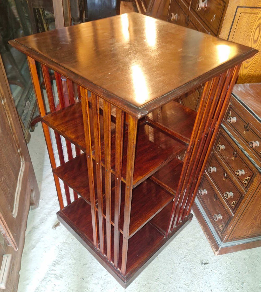 An Edwardian dark walnut revolving bookcase featuring a square moulded top, open internal tiers, and vertical slatted side supports. View IV