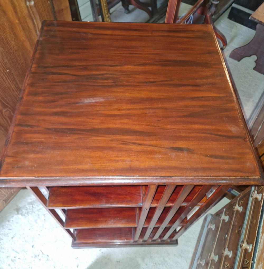 An Edwardian dark walnut revolving bookcase featuring a square moulded top, open internal tiers, and vertical slatted side supports. View V