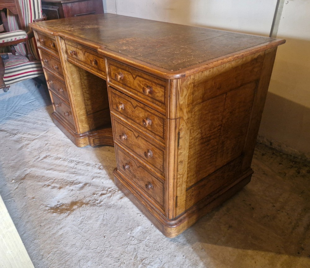A Victorian Hungarian ash pedestal writing desk featuring a worn leather top, turned wooden drawer knobs, and inlaid geometric crossbanding. View II