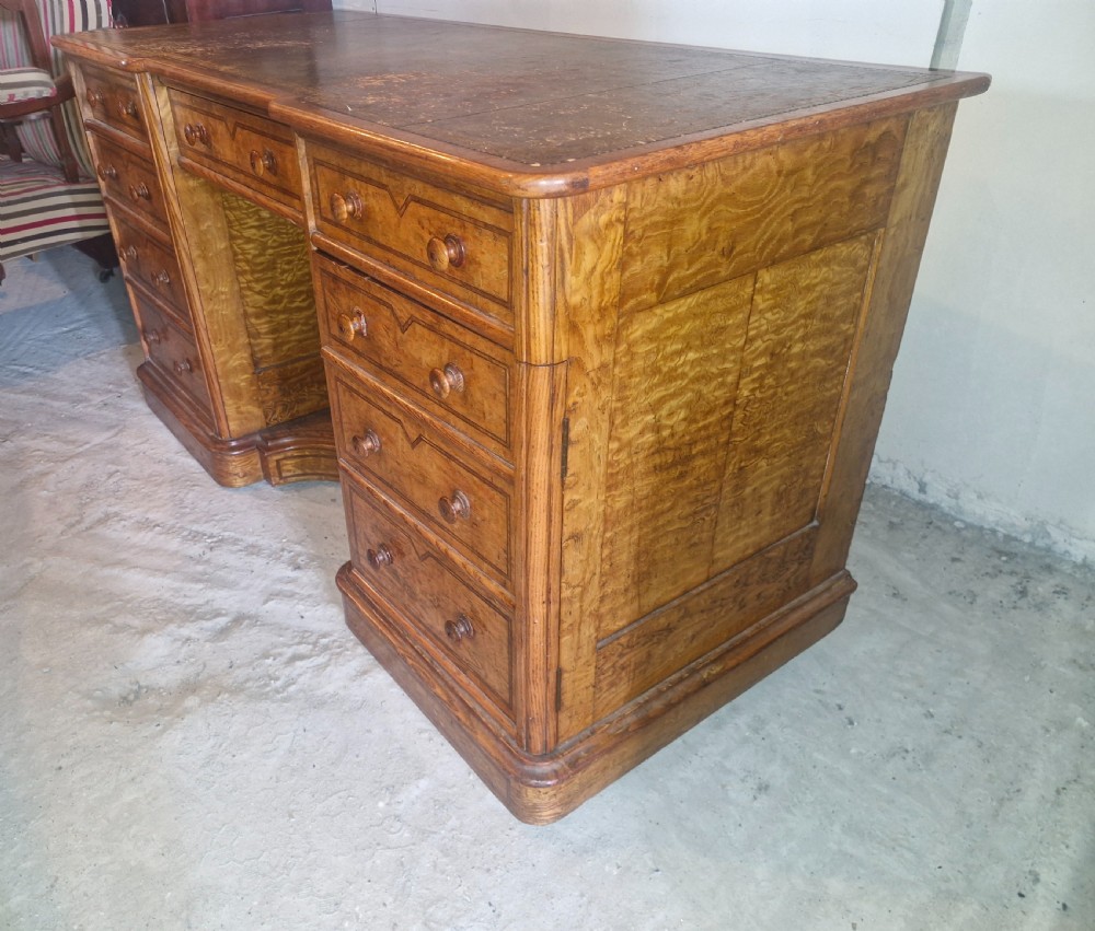 A Victorian Hungarian ash pedestal writing desk featuring a worn leather top, turned wooden drawer knobs, and inlaid geometric crossbanding. View IV