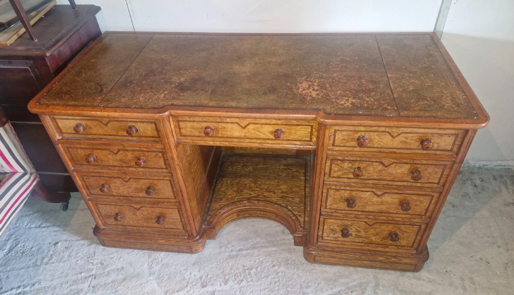 A Victorian Hungarian ash pedestal writing desk featuring a worn leather top, turned wooden drawer knobs, and inlaid geometric crossbanding. View V