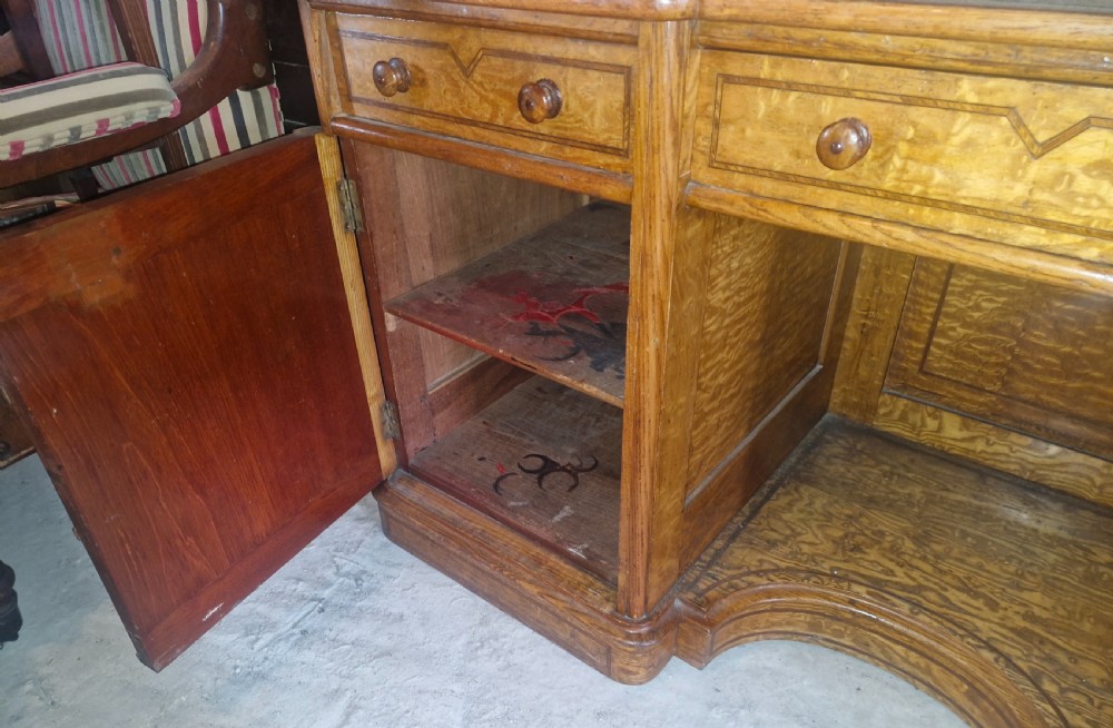 A Victorian Hungarian ash pedestal writing desk featuring a worn leather top, turned wooden drawer knobs, and inlaid geometric crossbanding. View VIII