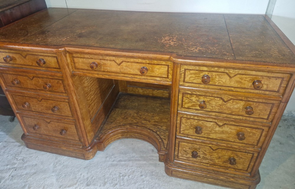 A Victorian Hungarian ash pedestal writing desk featuring a worn leather top, turned wooden drawer knobs, and inlaid geometric crossbanding. View IX