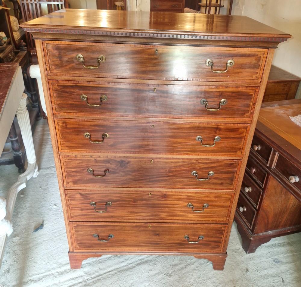 An Edwardian mahogany chest of six drawers featuring satinwood inlay banding, brass drop handles, and bracket feet.