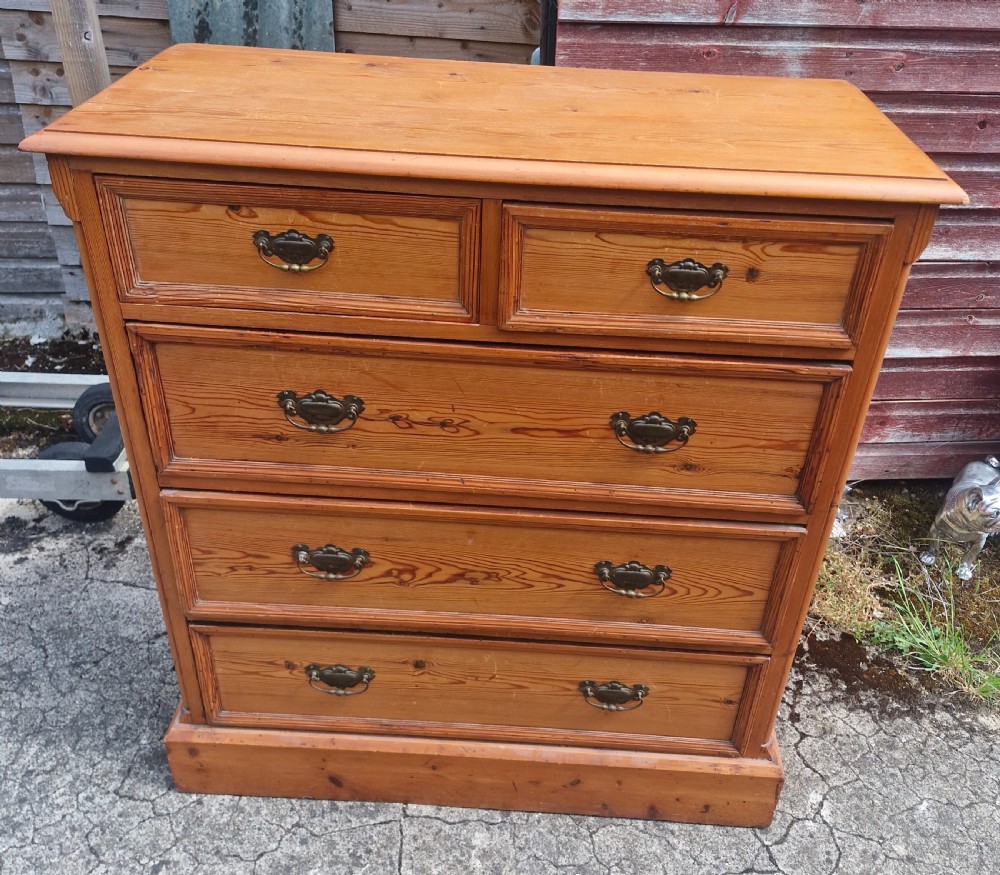An Edwardian pine chest of drawers featuring a two-over-three drawer configuration with brass drop handles and a plinth base.