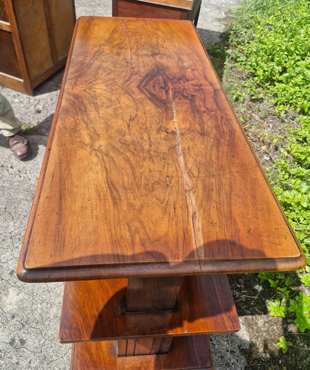 A three-tiered Victorian walnut adjustable buffet with carved lower supports resting outdoors on paved ground. View X