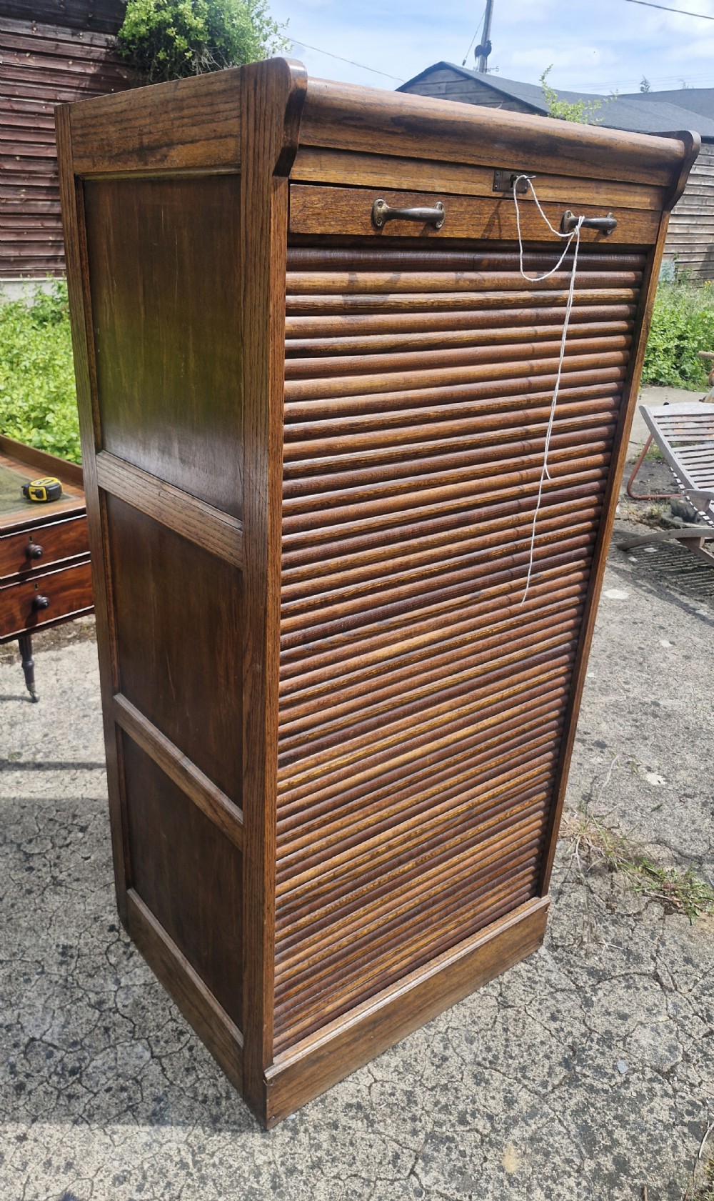 A tall early twentieth-century oak filing cabinet featuring a flexible vertical tambour roller shutter front with twin brass handles.
