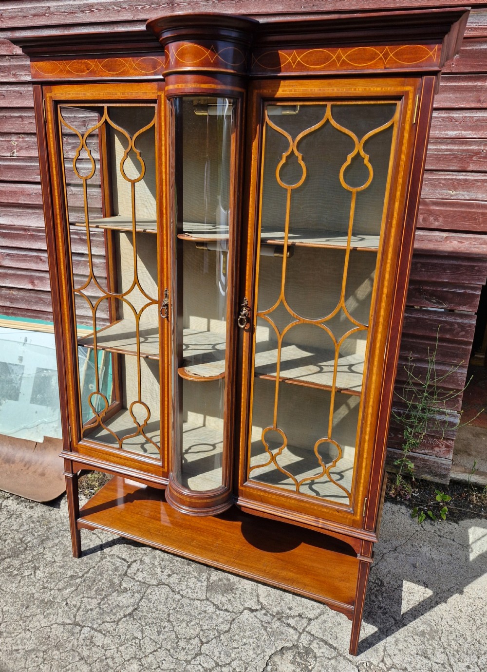An Edwardian mahogany display cabinet featuring astragal glazed doors, geometric satinwood inlay, a curved central glass section, and a lower undertier.