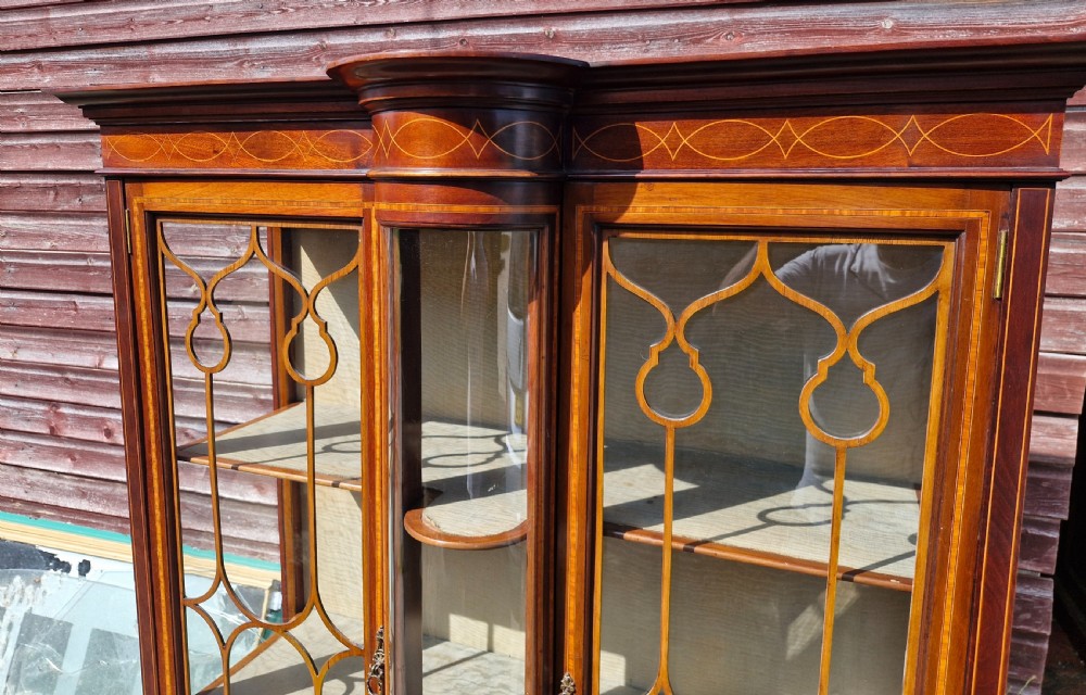 An Edwardian mahogany display cabinet featuring astragal glazed doors, geometric satinwood inlay, a curved central glass section, and a lower undertier. View IV