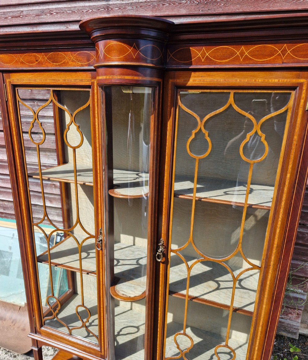 An Edwardian mahogany display cabinet featuring astragal glazed doors, geometric satinwood inlay, a curved central glass section, and a lower undertier. View VII