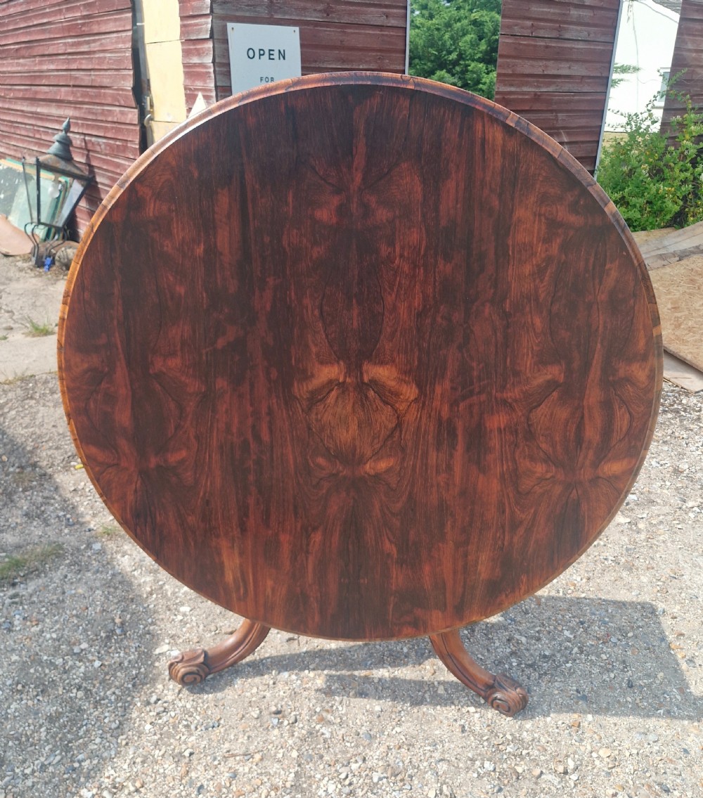 A mid-19th-century circular rosewood centre table shown tilted vertically to display its symmetrical figured grain and carved pedestal base.