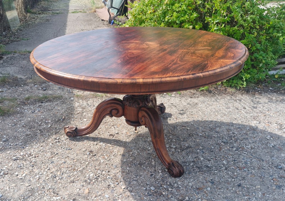 A mid-19th-century circular rosewood centre table shown tilted vertically to display its symmetrical figured grain and carved pedestal base. View VI