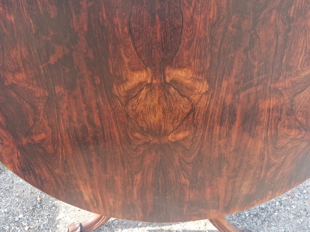 A mid-19th-century circular rosewood centre table shown tilted vertically to display its symmetrical figured grain and carved pedestal base. View VIII