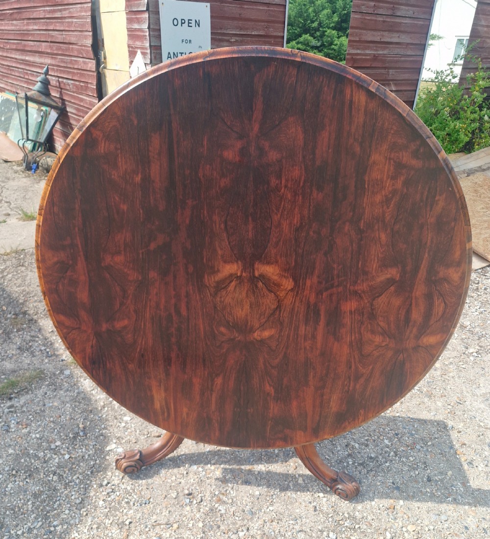 A mid-19th-century circular rosewood centre table shown tilted vertically to display its symmetrical figured grain and carved pedestal base. View X