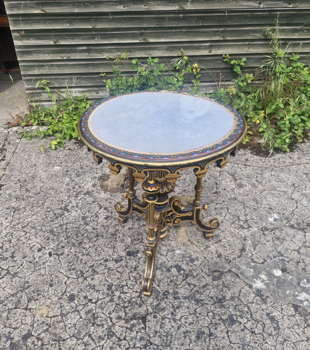 A nineteenth-century circular occasional table featuring a blue fabric inlay top surrounded by polychrome and gilt painting on an ebonised carved pedestal base.