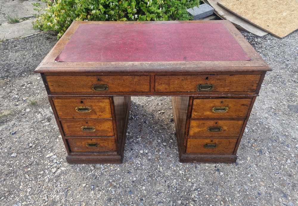A late Victorian oak kneehole pedestal writing desk featuring a red leather writing surface, multiple drawers, and recessed flush brass handles.