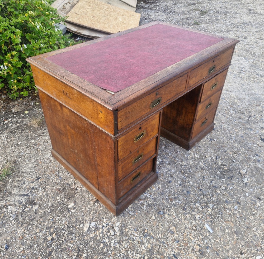 A late Victorian oak kneehole pedestal writing desk featuring a red leather writing surface, multiple drawers, and recessed flush brass handles. View III