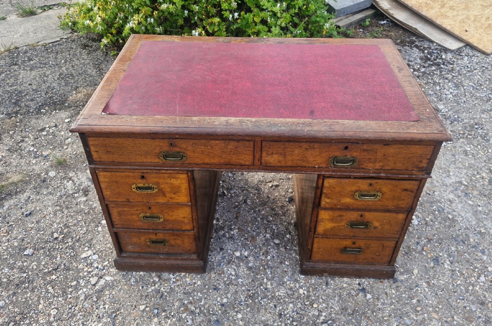 A late Victorian oak kneehole pedestal writing desk featuring a red leather writing surface, multiple drawers, and recessed flush brass handles. View IV