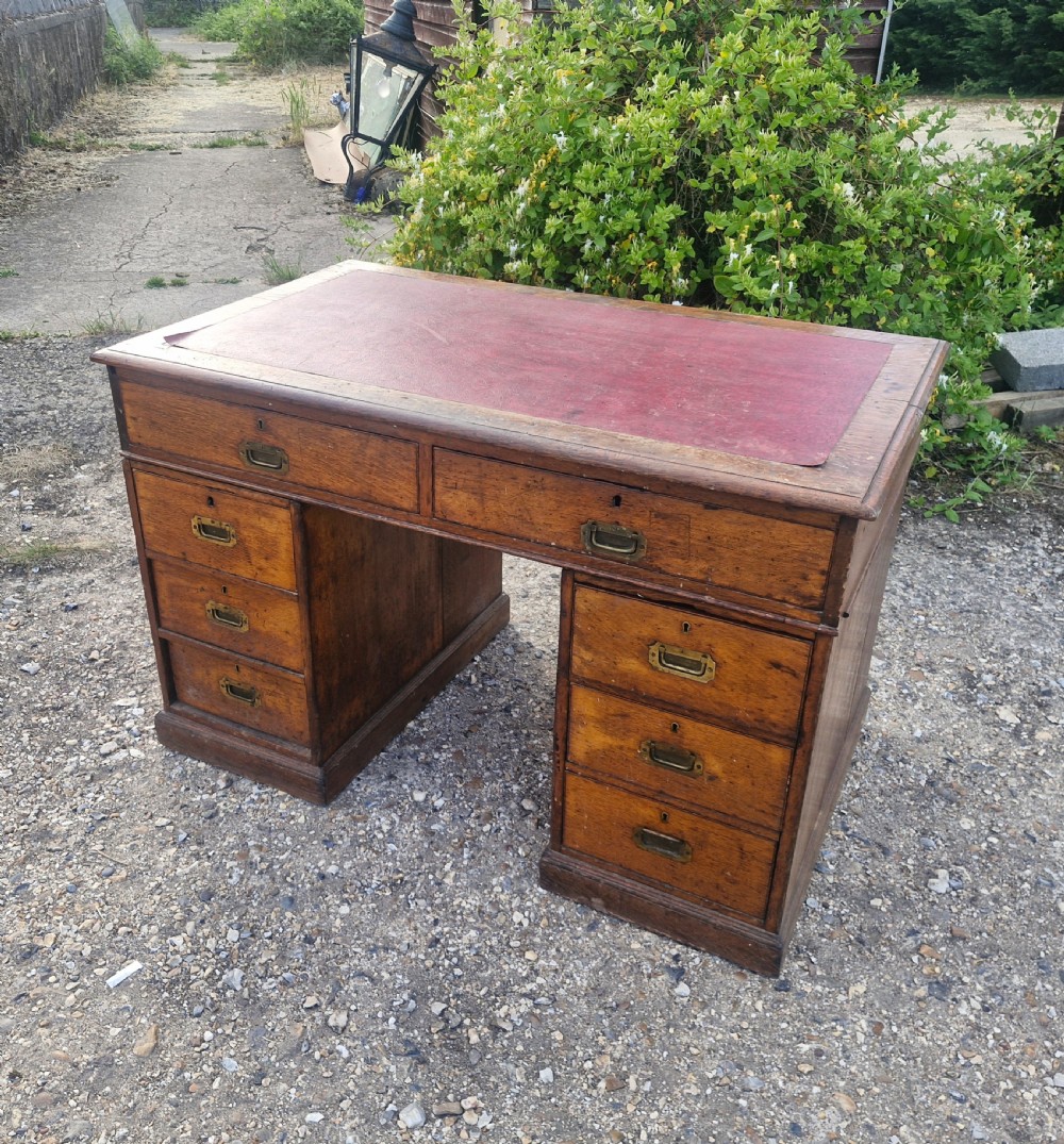 A late Victorian oak kneehole pedestal writing desk featuring a red leather writing surface, multiple drawers, and recessed flush brass handles. View V