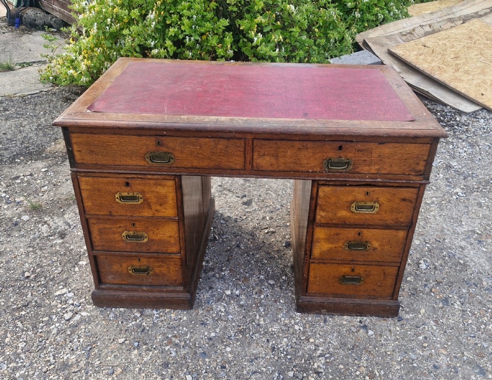 A late Victorian oak kneehole pedestal writing desk featuring a red leather writing surface, multiple drawers, and recessed flush brass handles. View VI