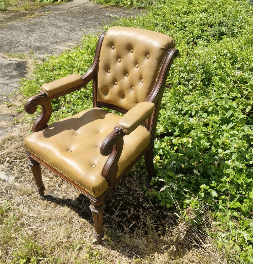 A mid-19th century mahogany desk armchair with tan button-tufted upholstery, scroll carved armrests, fluted front legs, and castors. View IV