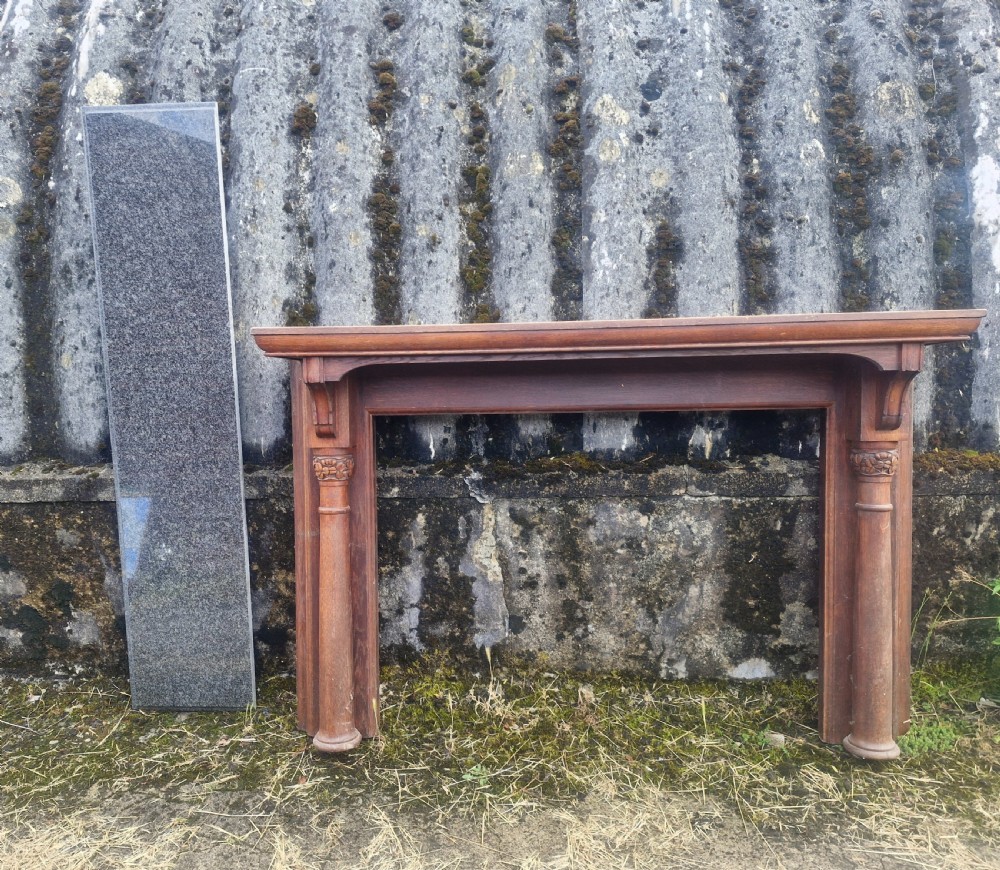 An Edwardian carved oak fire surround featuring twin column supports alongside a long polished dark granite hearth slab.