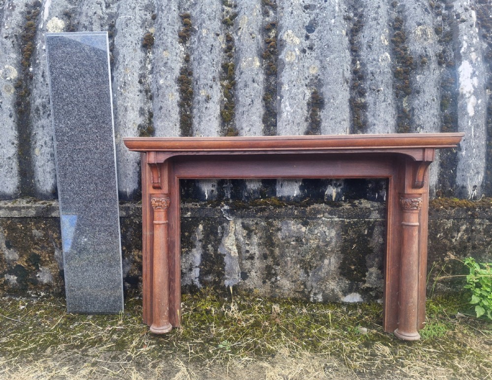 An Edwardian carved oak fire surround featuring twin column supports alongside a long polished dark granite hearth slab. View II