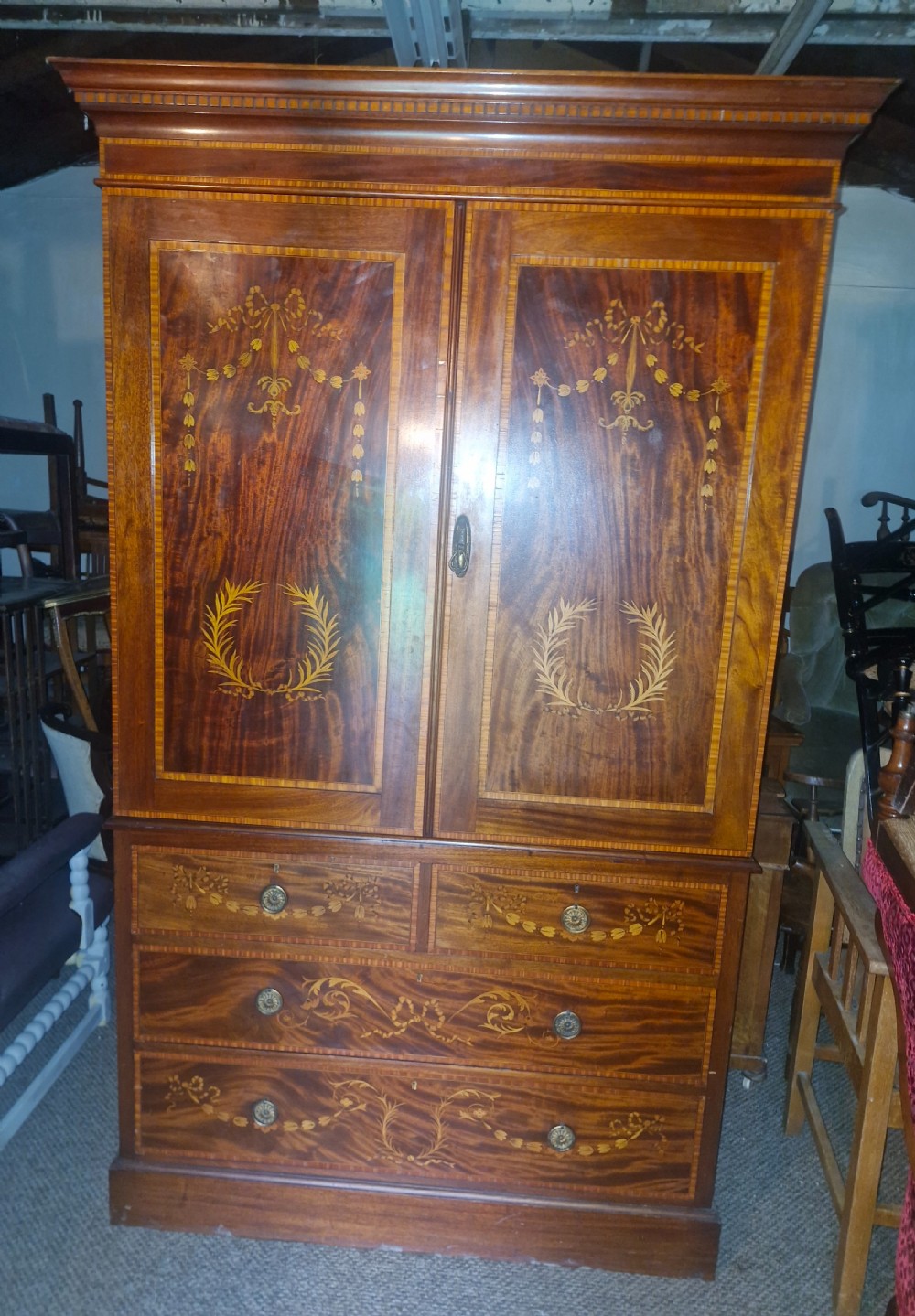An Edwardian mahogany linen press featuring satinwood marquetry swags and laurel wreaths on the double doors above four drawers.