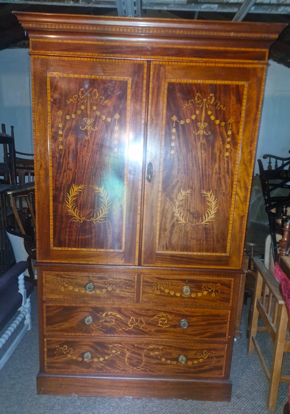 An Edwardian mahogany linen press featuring satinwood marquetry swags and laurel wreaths on the double doors above four drawers. View VII