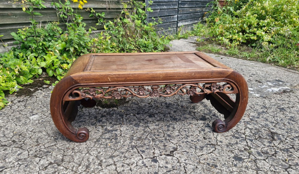 A low rectangular warm brown hardwood Chinese opium table featuring carved floral aprons and curved scroll legs.