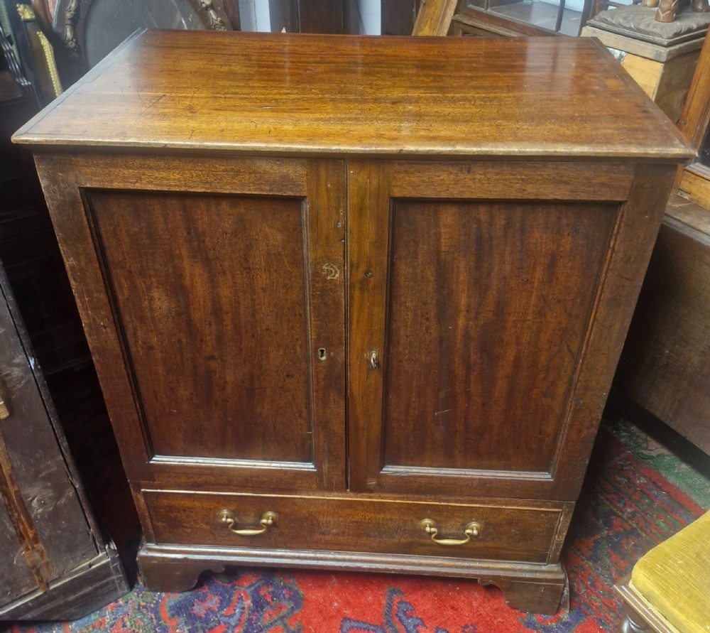 A late Georgian mahogany cupboard with two panelled doors positioned over a single wide drawer with twin brass handles, resting on bracket feet. View II