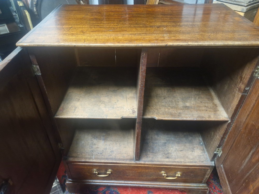 A late Georgian mahogany cupboard with two panelled doors positioned over a single wide drawer with twin brass handles, resting on bracket feet. View IV