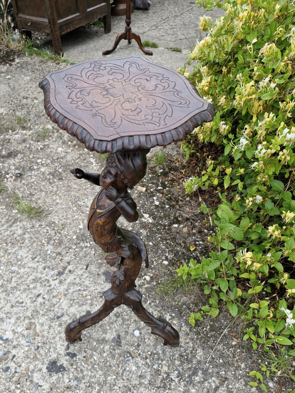 A late 19th-century carved dark walnut gueridon stand featuring a scalloped top supported by a carved figurative stem on a tripod base. View IV