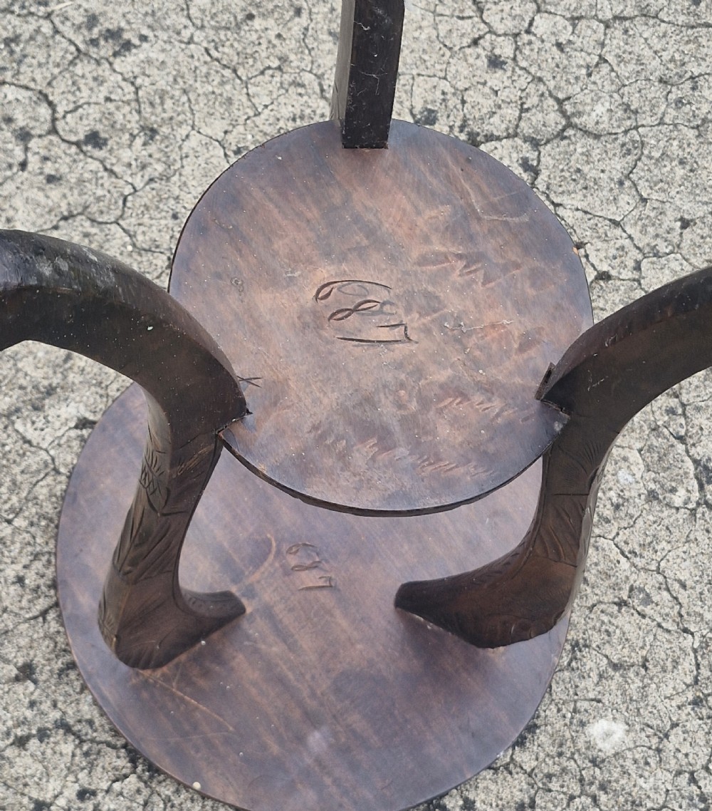 A dark brown carved wood two-tier occasional table with floral leaf carvings on the circular top and lower shelf, supported by four curved legs. View II